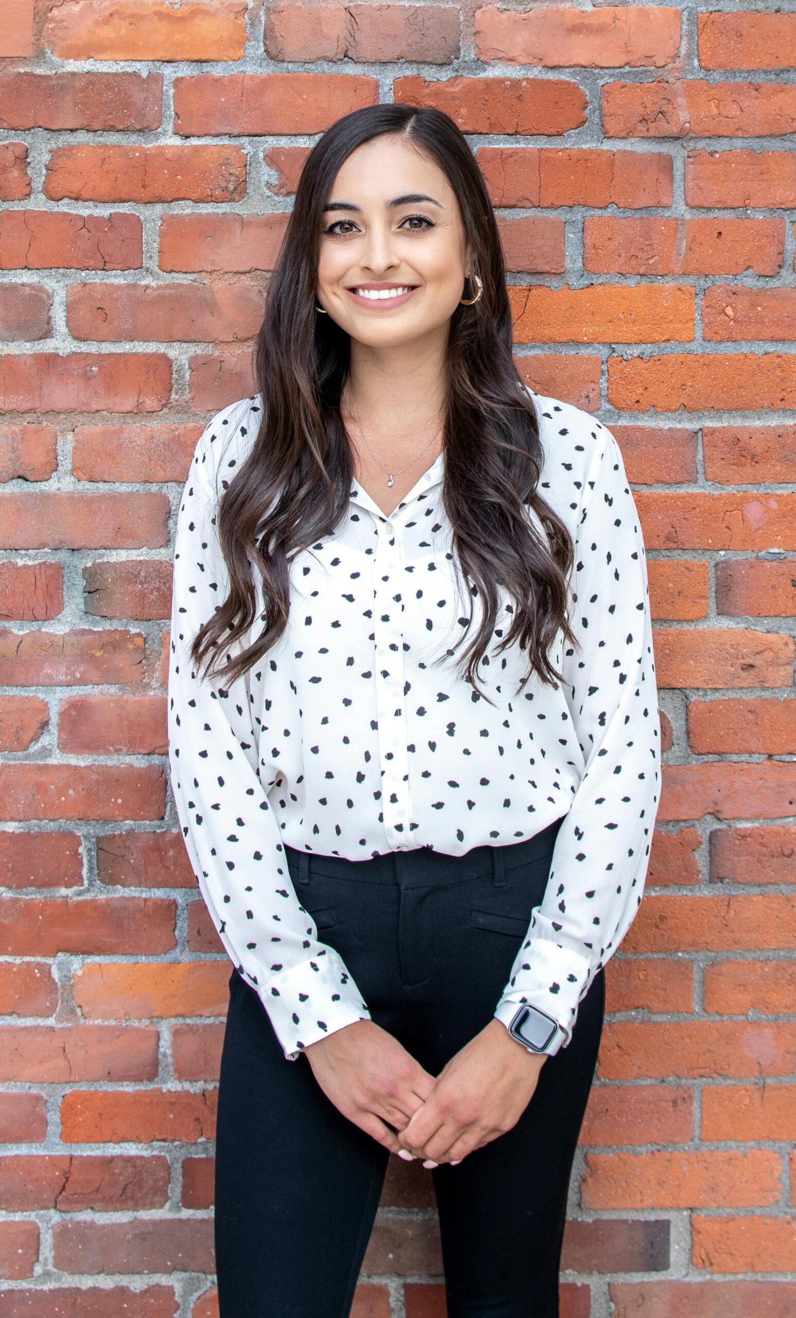 Confident young business woman standing against a red brick wall, smiling.