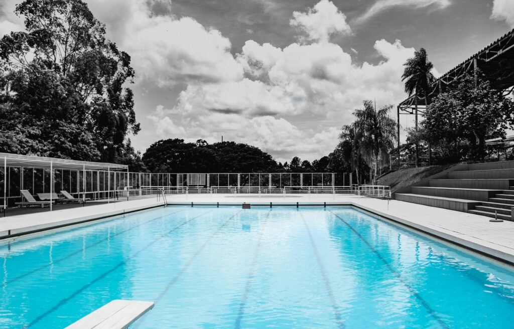 Tranquil outdoor swimming pool surrounded by lush trees and modern architecture under a vibrant sky.